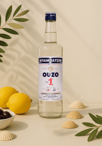 In der Mitte steht eine Flasche Ouzo und vor einer Wand. Neben dran liegen dekoartikel wie eine Zintrone und Oliven.